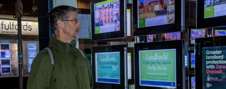 A middle aged male landlord is pictured looking into an estate agents window as he ponders selling his property.